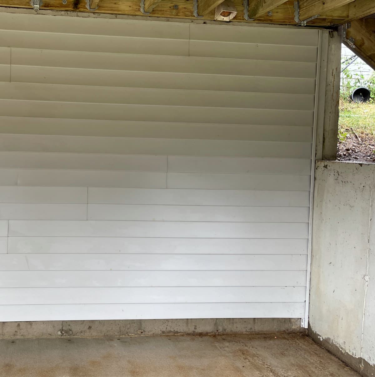 Vinyl house siding being soft-washed, the lower courses back to clean white