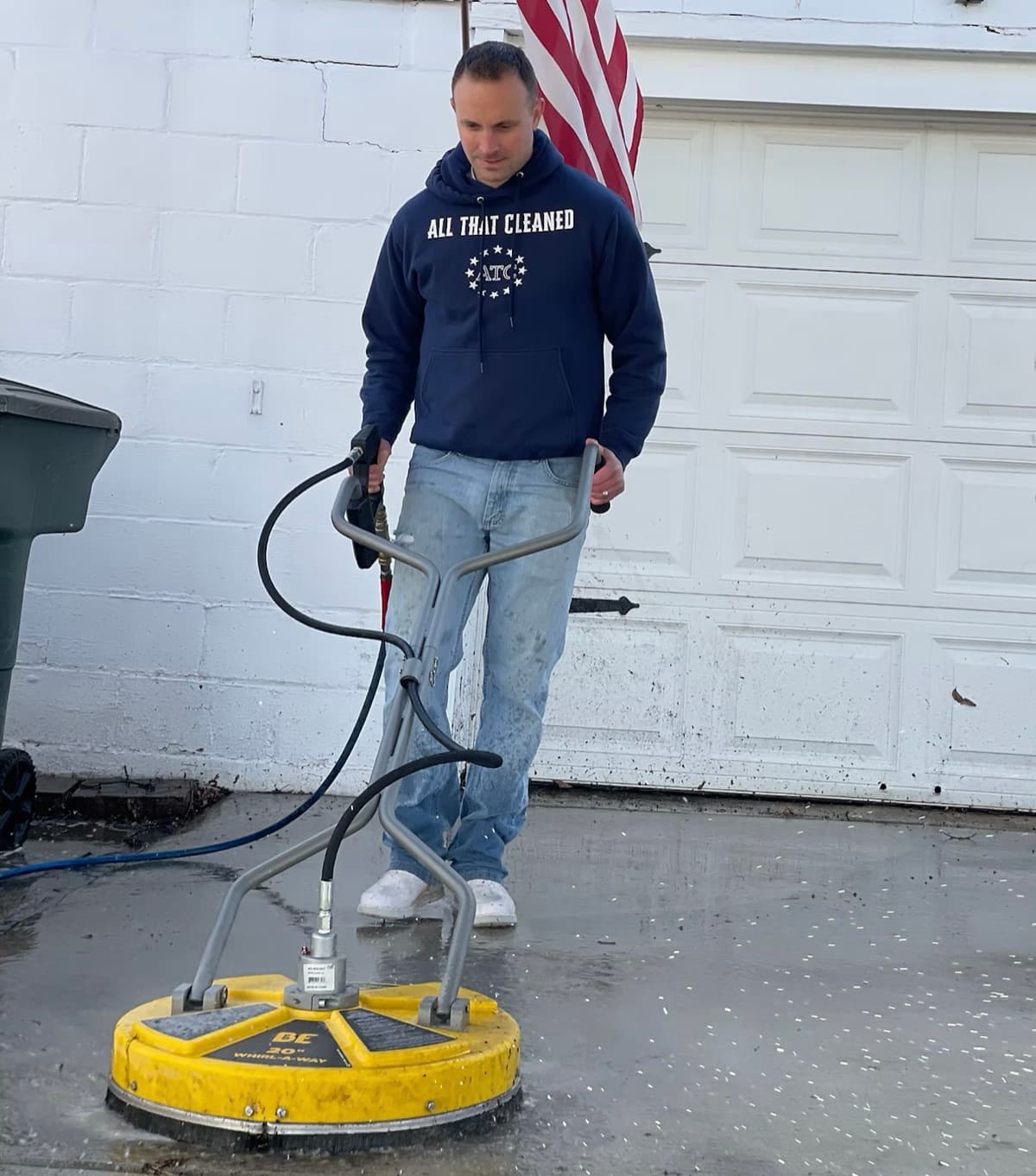 ATC owner in a branded hoodie running a 20-inch surface cleaner across a residential driveway